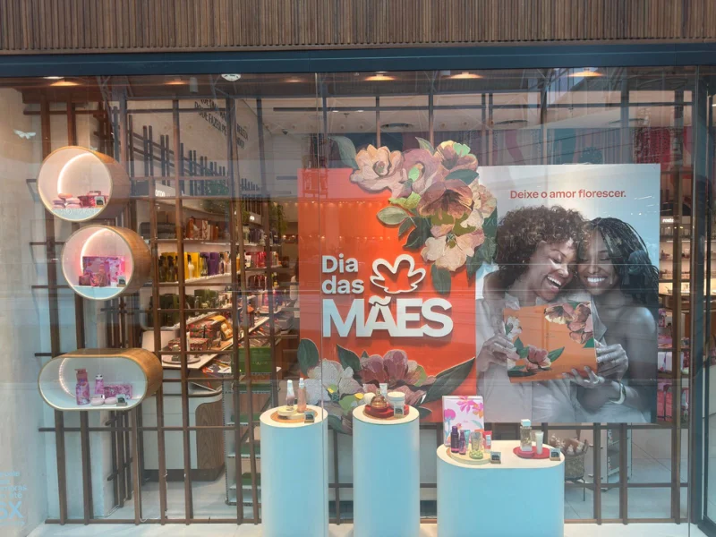 Vitrine da loja Natura com a campanha do dia das mães com duas mulheres negras se abraçando e alguns kits de produtos como sugestão de presente.