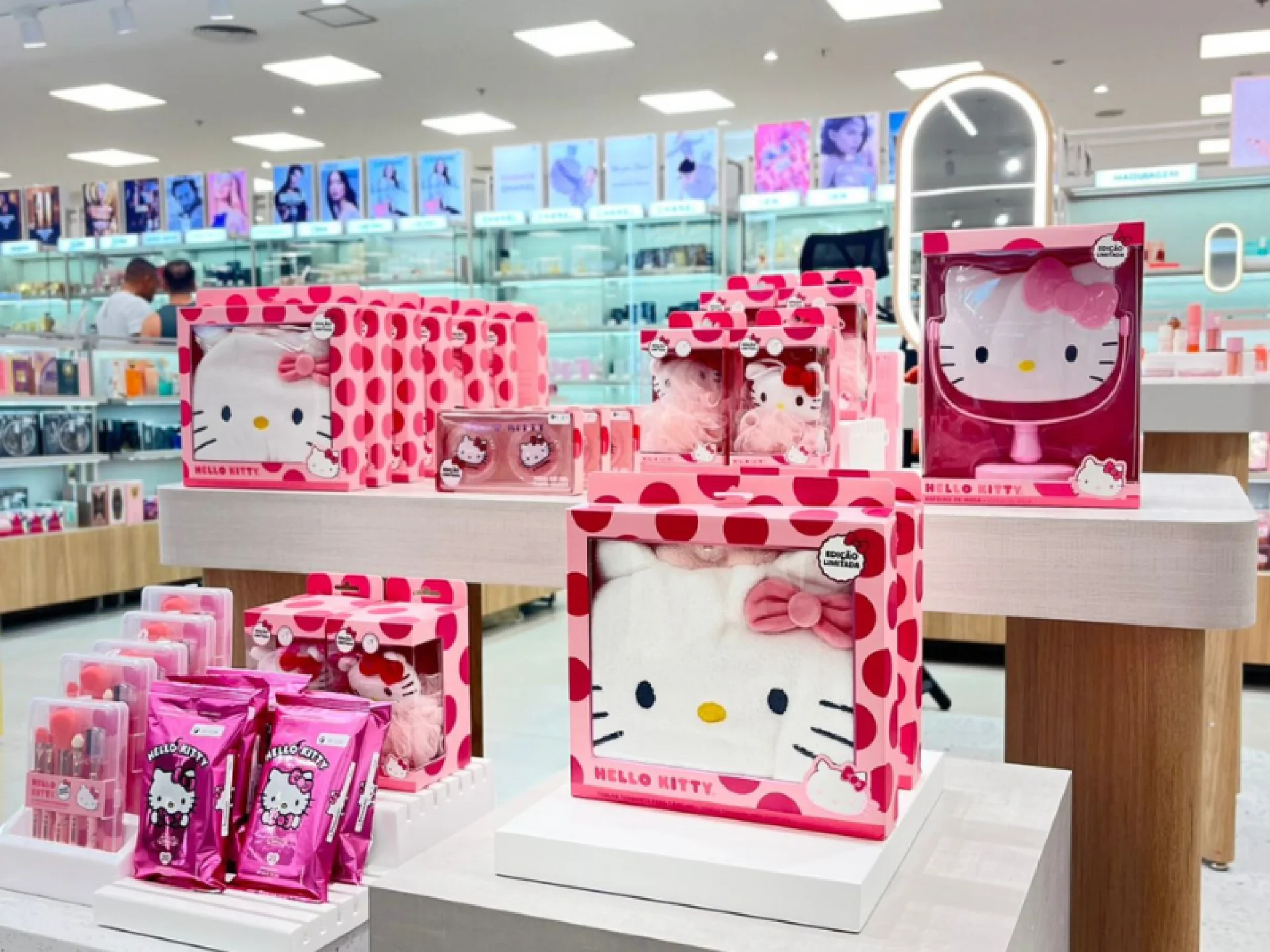 Produtos de beleza temáticos da hello kit, arrumados em três balcões de madeira. Dentre os produtos tem esponja de tomar banho, espelho para maquiagem, demaquilante, pincéis de maquiagem, touca para proteger o cabelo.