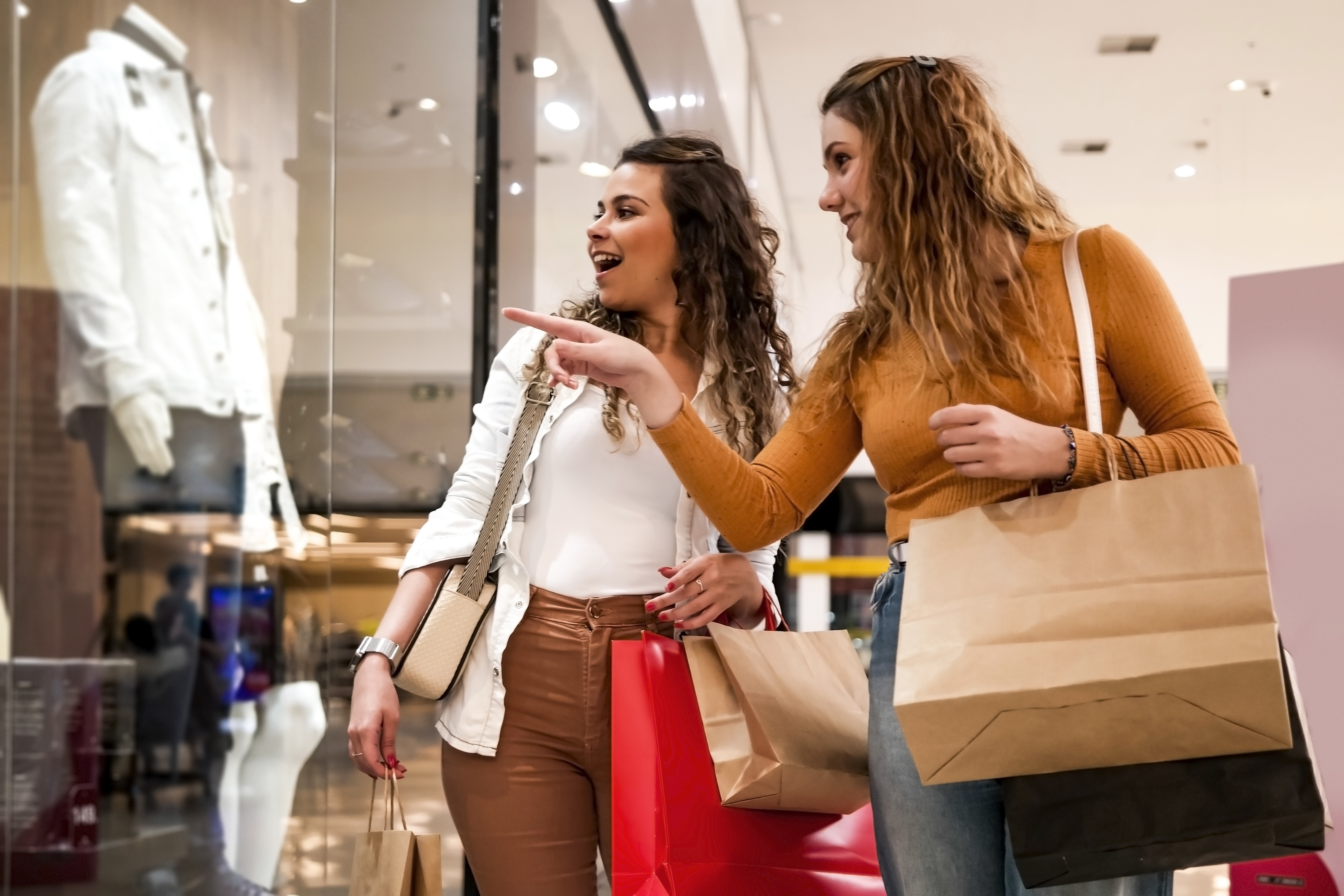 Duas mulheres olhando vitrine com sacolas de compras em mãos.